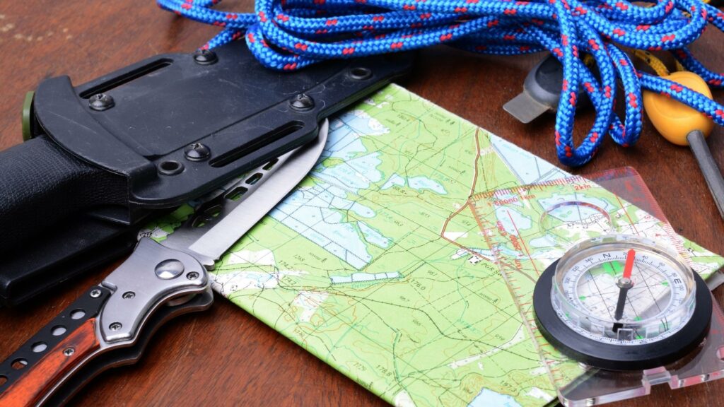 Survival tools that include a map, compass, knife, and rope all on a table 
