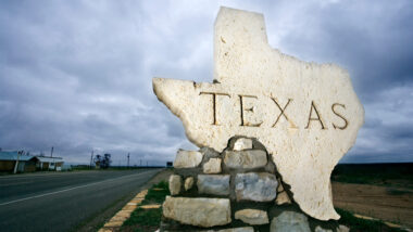 A rock shaped in the shape of Texas with the state on it on the side of a road.