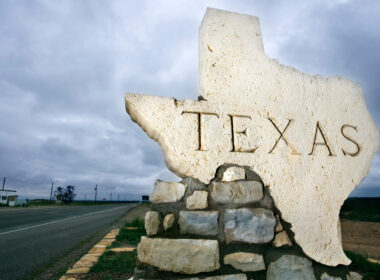 A rock shaped in the shape of Texas with the state on it on the side of a road.
