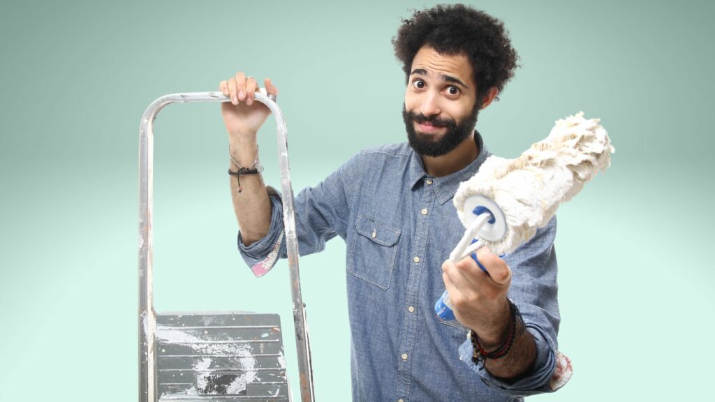 A man holding a ladder and a paint brush with a silly look on his face