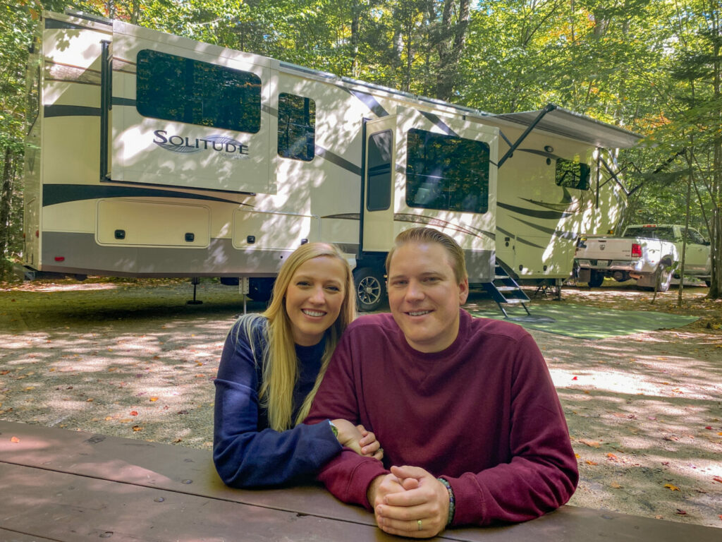 A couple sitting at a picnic table with their RV in the background. They have been living fulltime in a RV for years. 