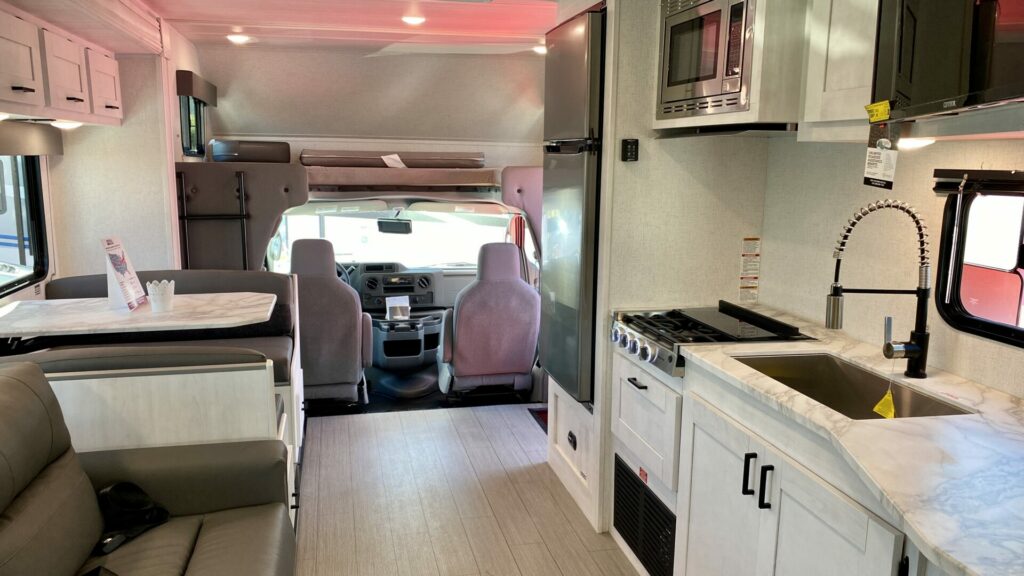Interior of a new RV showing the kitchen, dining area, couch, and driving area. 
