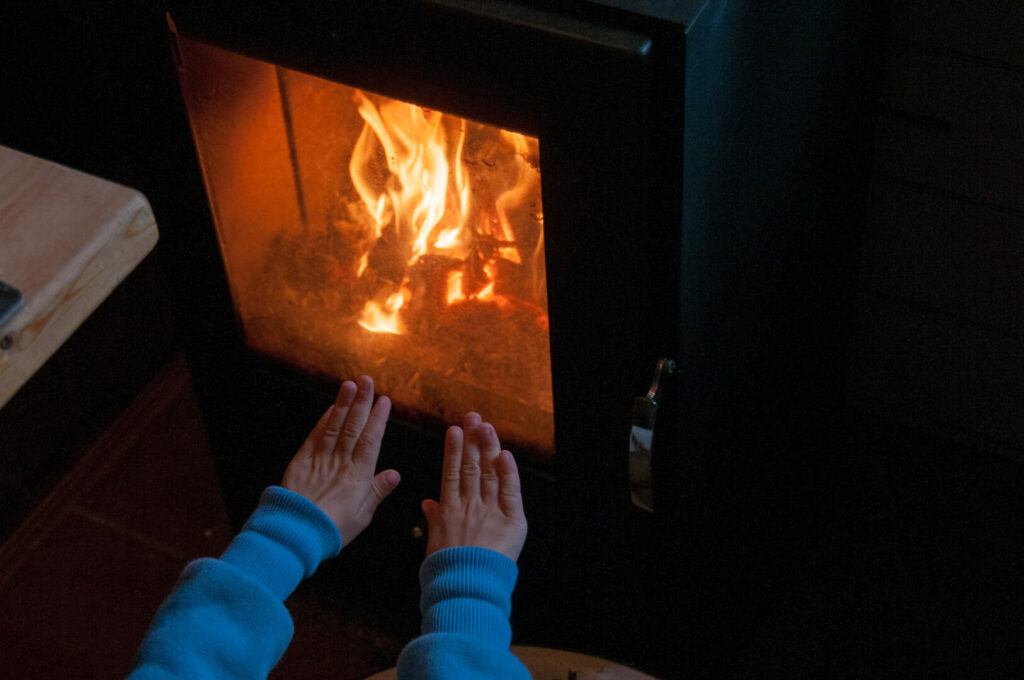 A person putting their hands up near their RV wood stove to stay warm