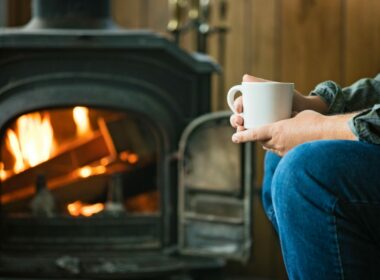Person sitting near their RV wood stove with a hot drink