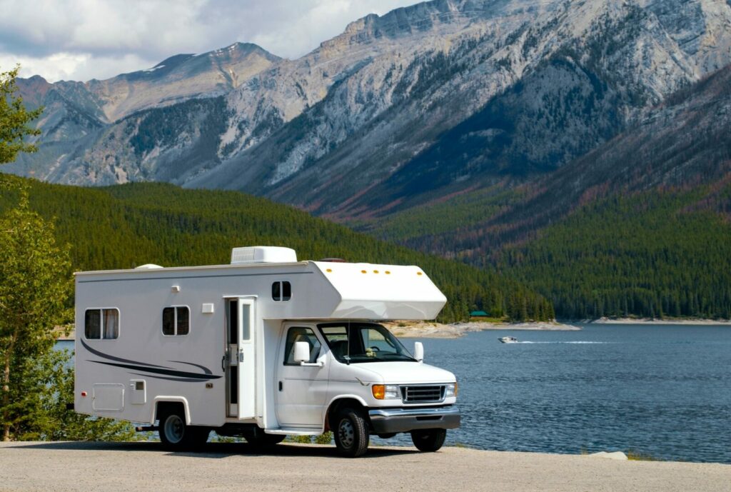 An RV parked by the water near the mountains after deciding to sleep here instead of not knowing if they can sleep at a rest stop