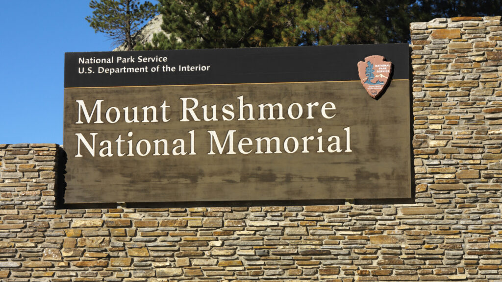 An entry sign for mount rushmore national memorial, where many believe there is a 5th hidden face