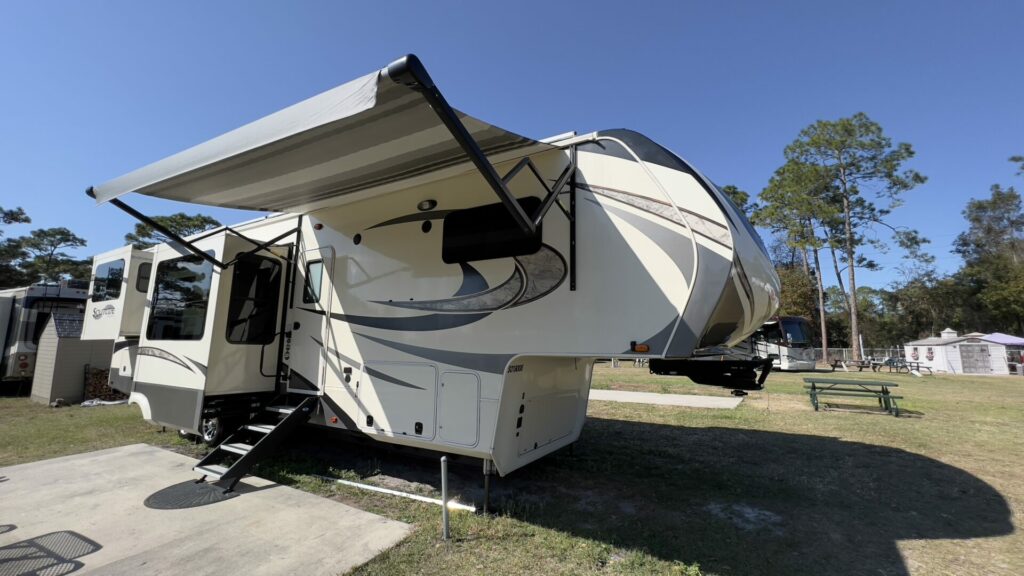 An fifth wheel RV parked in a campsite with the awning out and all clean, ready to sell