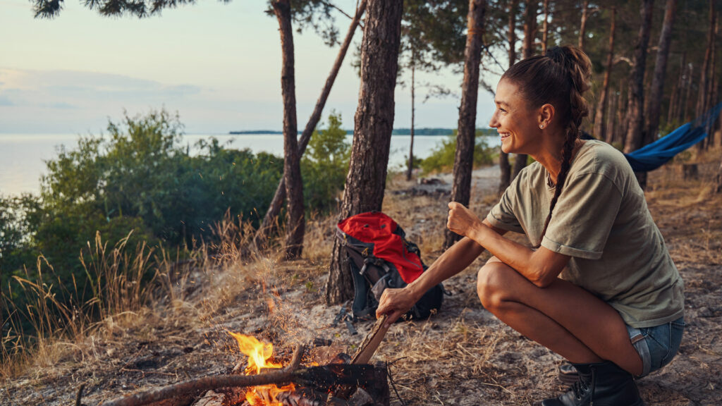 A woman starting a campfire, fully prepared for emergencies with her RV fire extinguisher