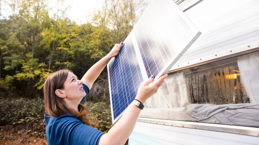 A woman lifting her foldable solar panel in the air to try and get more sun on it near her RV.