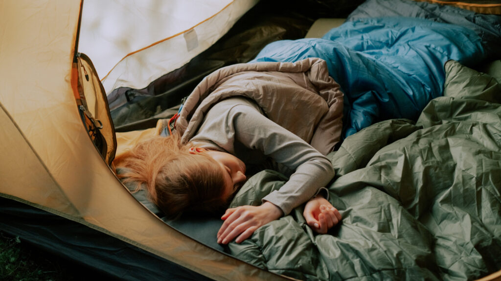 A woman sleeping in her tent with one of the best camping blankets