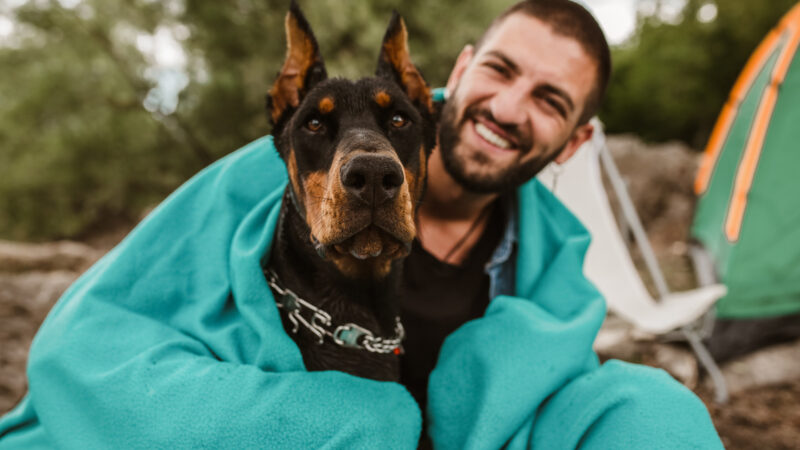 A man and his dog cuddled up in one of the best camping blankets