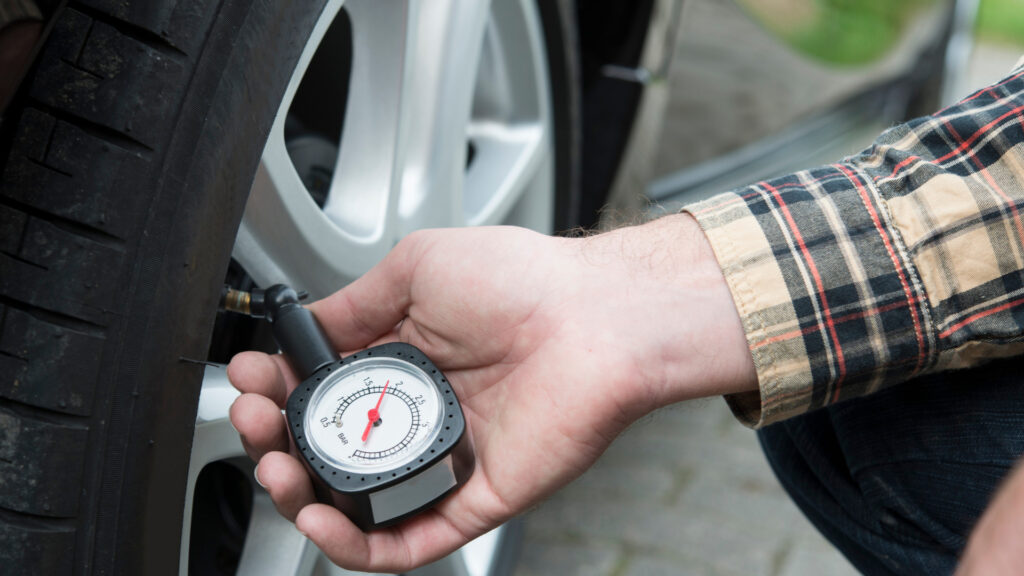 A person checking their tire pressure to reduce fuel usage and to secure the lowest gas prices in usa
