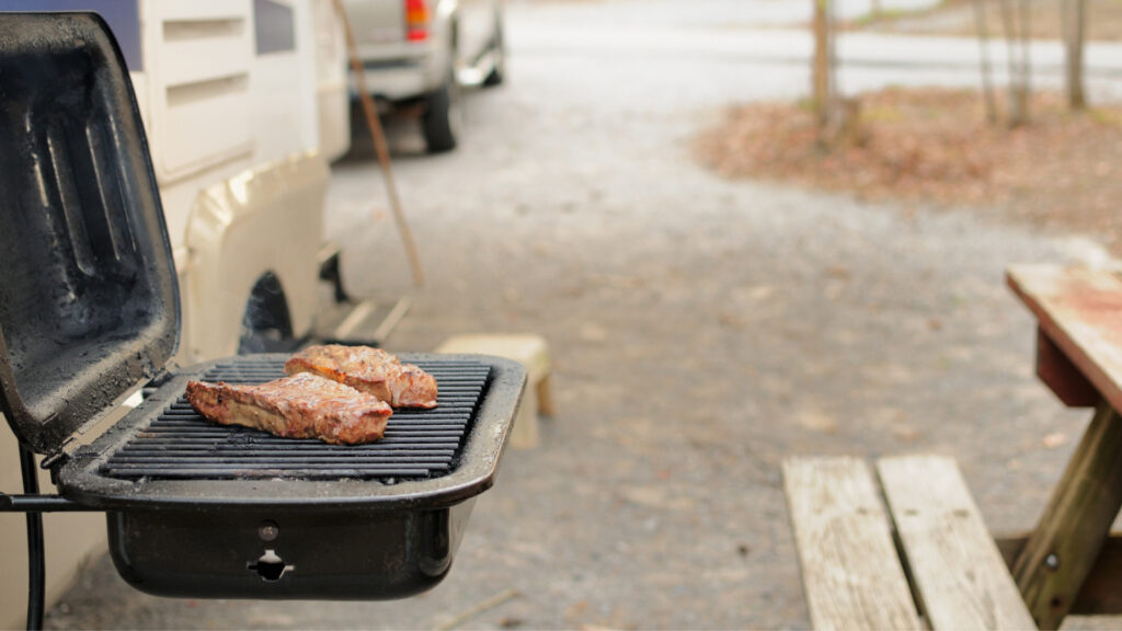 Meat cooking on a grill near an RV at a campsite