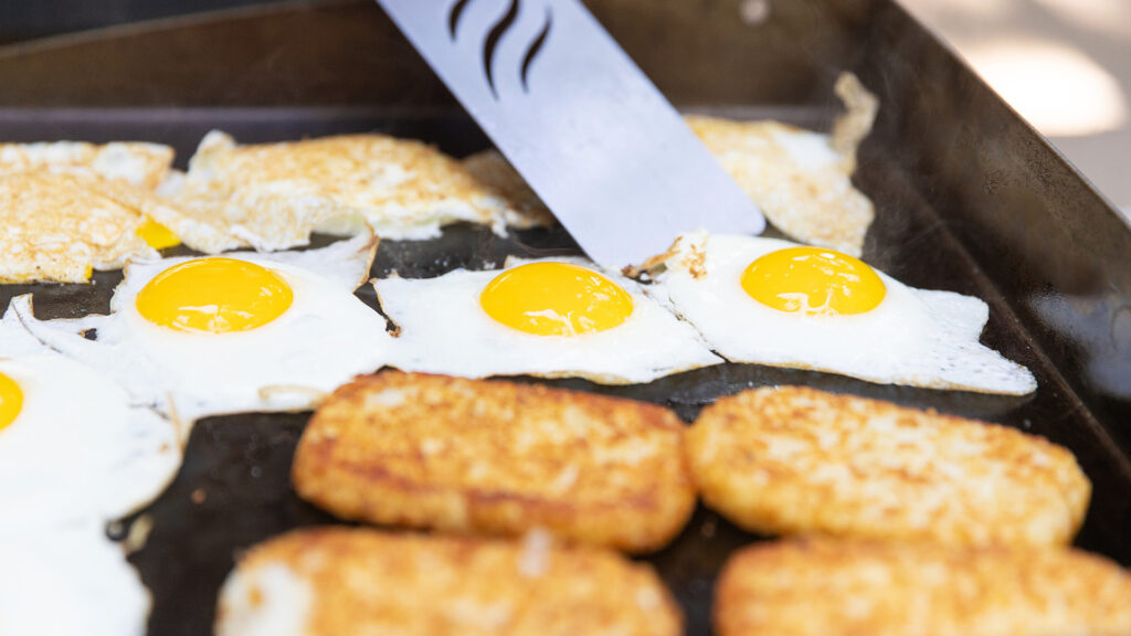 A person cooking eggs and hash browns on a griddle