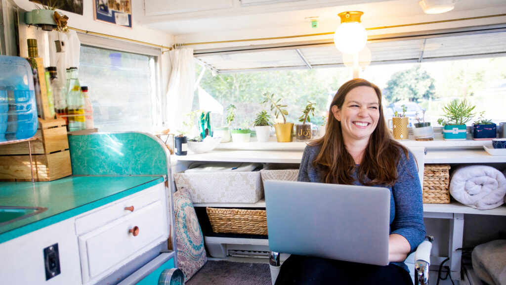 A woman sitting in her RV typing on her laptop  that uses azdel panels
