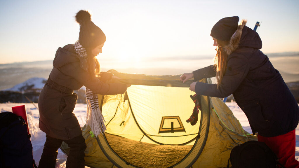 Friends following a winter tip and putting up their tent to keep themselves warm while winter camping
