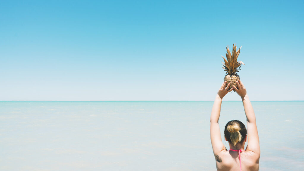 A woman holding a pineapple by the beach after learning the meaning of upside down pineapple