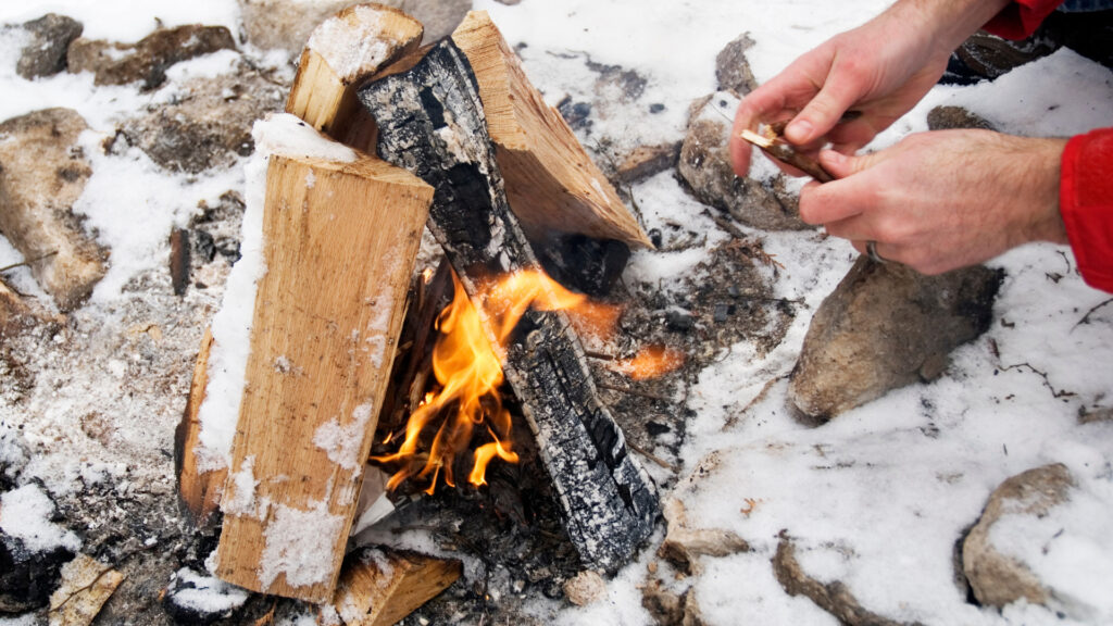 A person starting a fire in the snow, following five rules for the perfect campfire