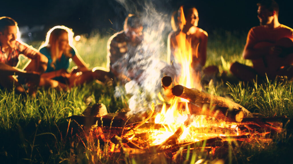 A group sitting around a campfire at night that was started by following five rules for the perfect campfire