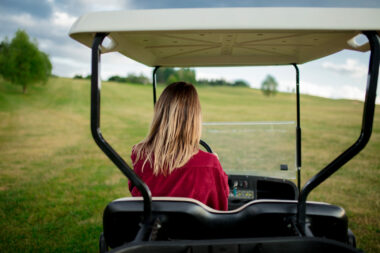 A woman driving in her golf cart that she brought to a golf course using a golf cart carrier