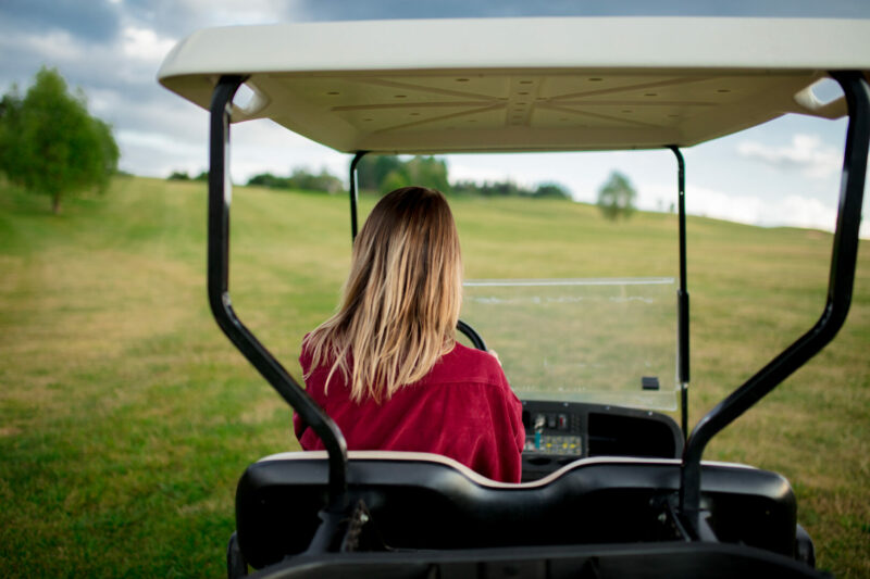 A woman driving in her golf cart that she brought to a golf course using a golf cart carrier