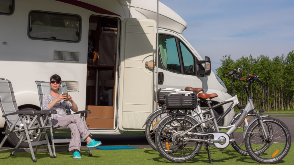 A woman sitting next to her RV and bikes that she brought along using an RV ladder bike rack