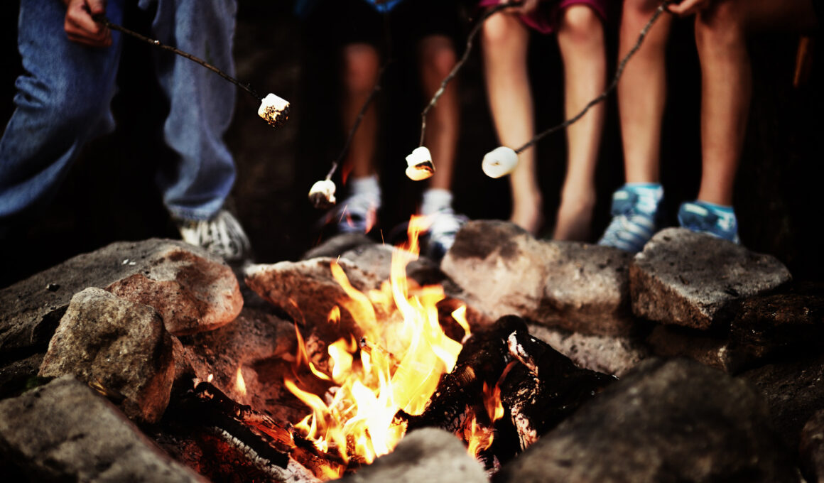 A group roasting marshmallows around a campfire at night that was started by following five rules for the perfect campfire