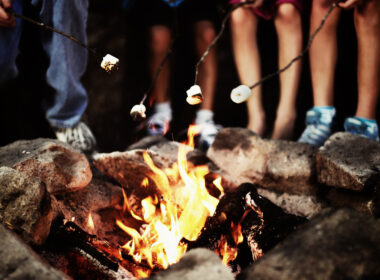 A group roasting marshmallows around a campfire at night that was started by following five rules for the perfect campfire