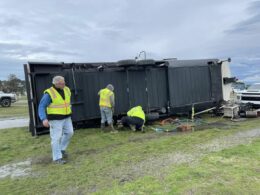 an RV that was flipped in the wind with men in safety vests walking around it