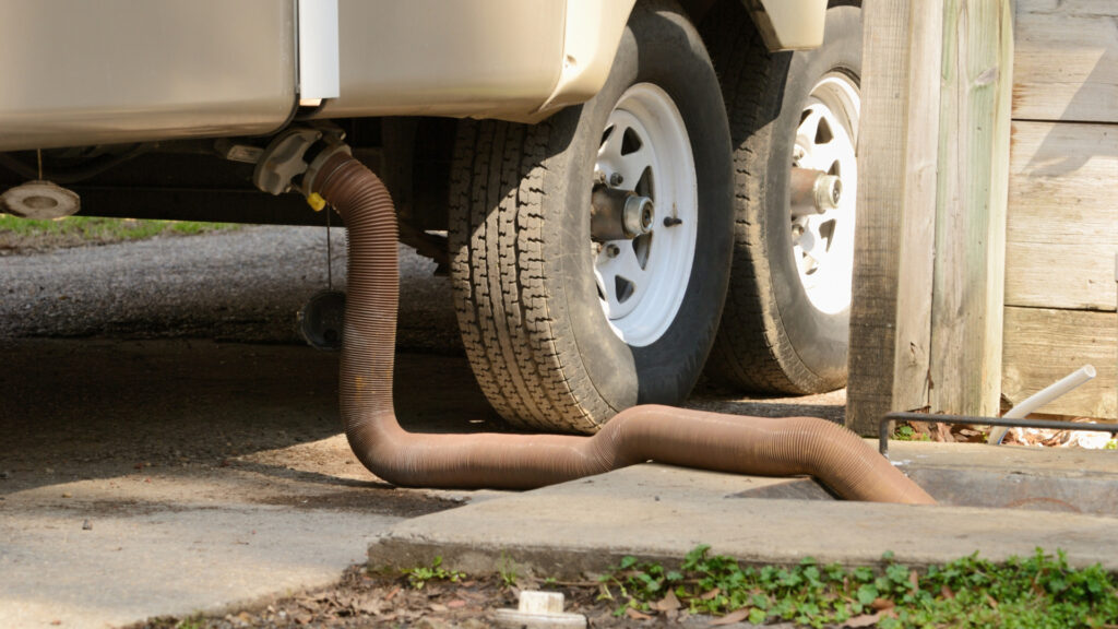 An RV parked at a dump station with the sewer hose connected and draining