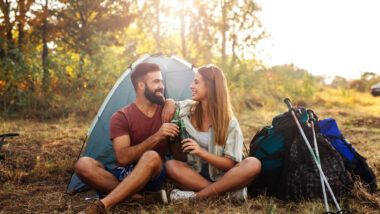A couple drinking outside of their camping tent with an air conditioner