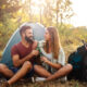 A couple drinking outside of their camping tent with an air conditioner