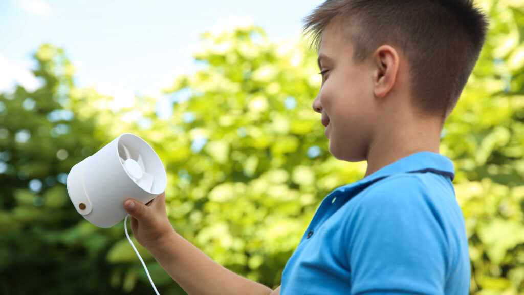 A boy using a portable fan outside of his camping tent