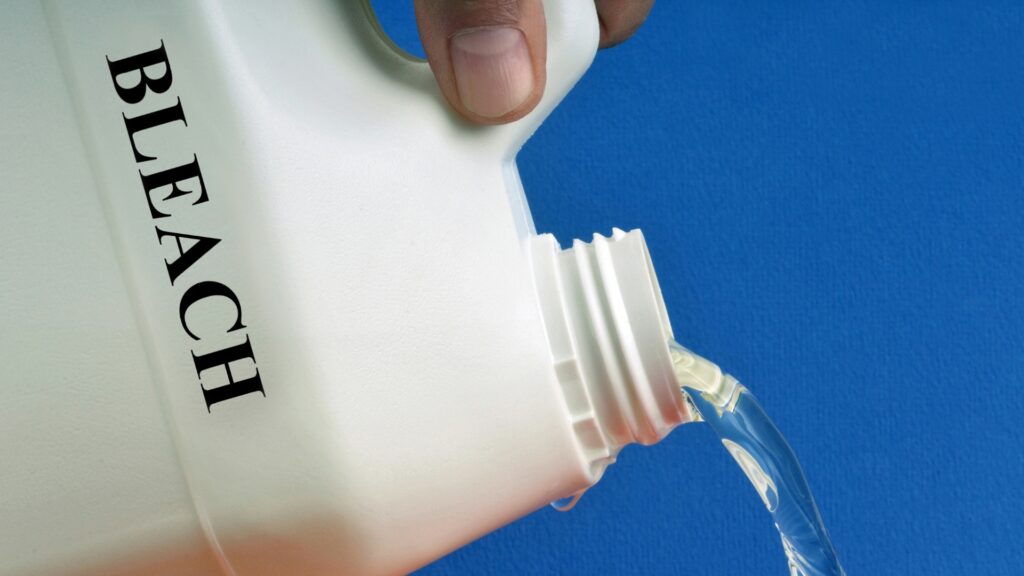 A hand pouring a white bottle with the word "bleach" written on it 
