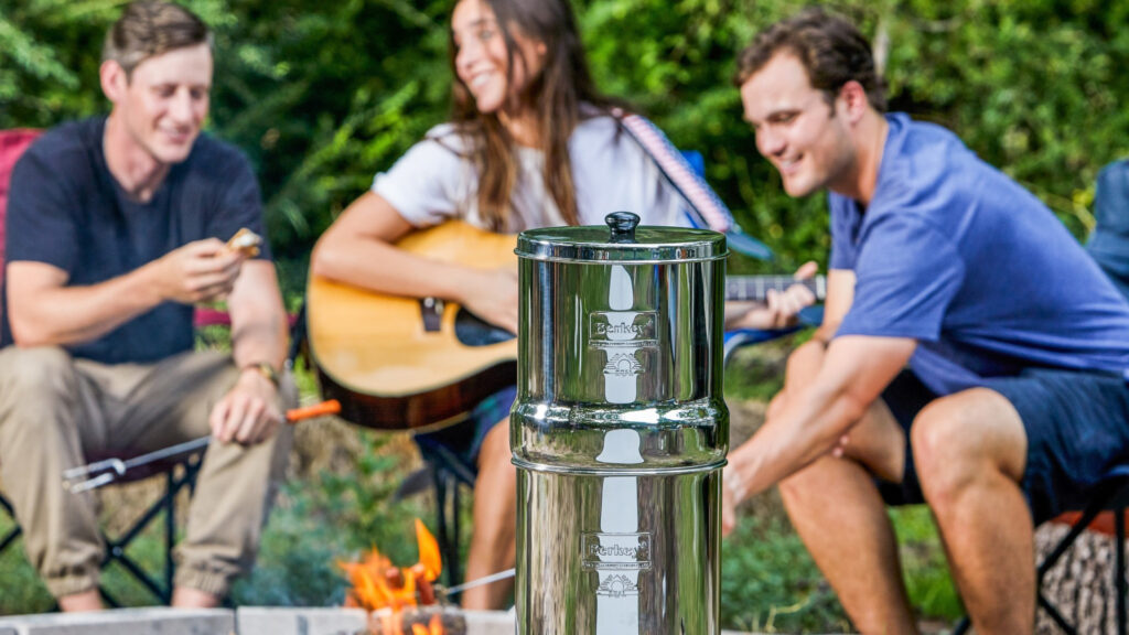 A group of friends sitting around a campfire by their travel Berkey water filter