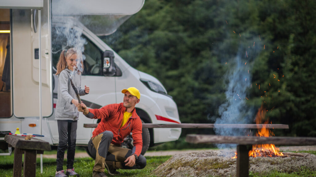 A father and daughter starting a campfire outside of their RV