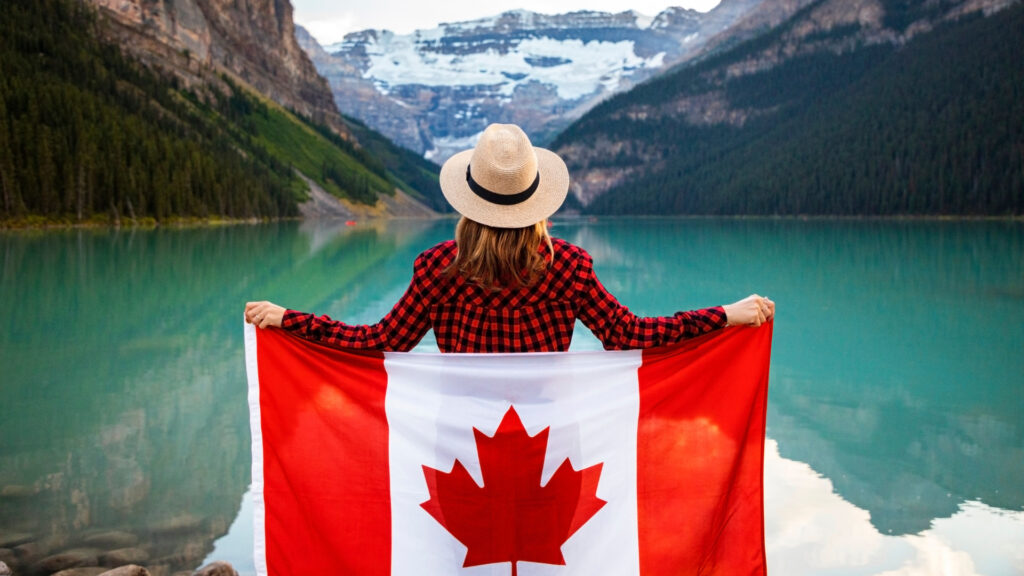 A woman standing in the mountains in Canada holding a Canadian Flag behind her