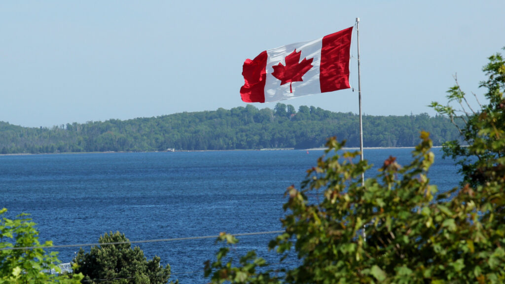 A Canadian flag waving by a lake