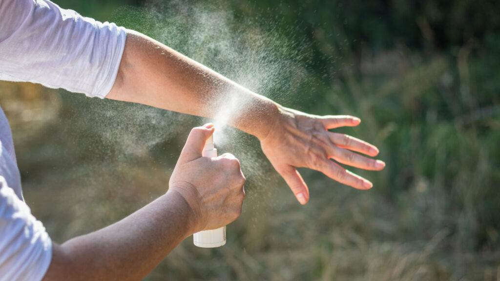 A person spraying on mosquito repellent