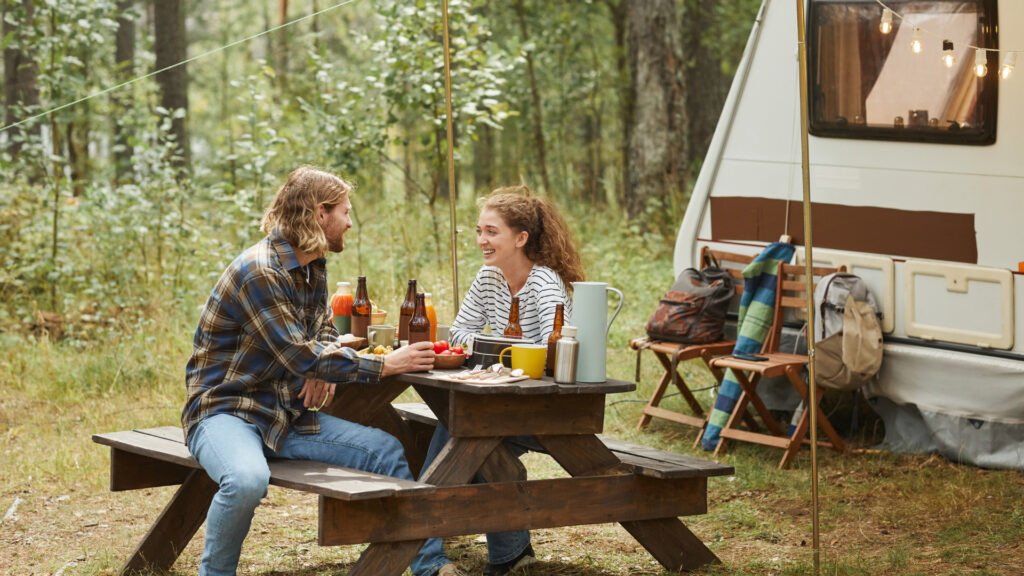 A couple drinking beer outside of their RV at their campsite secured using their escape membership