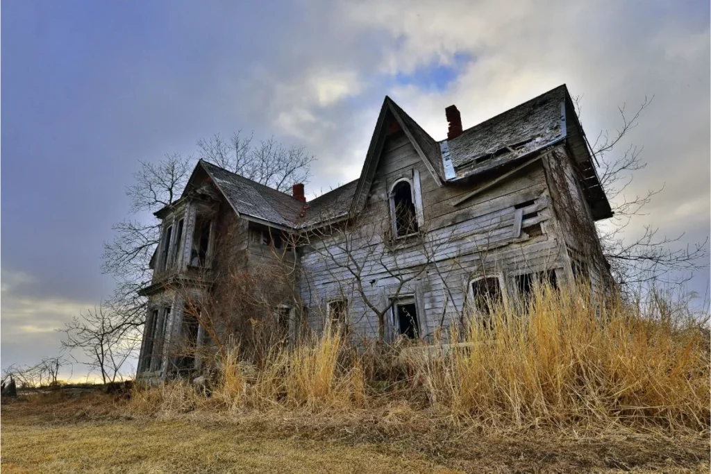 An old house missing doors and windows in an abandoned place with an overgrown field.