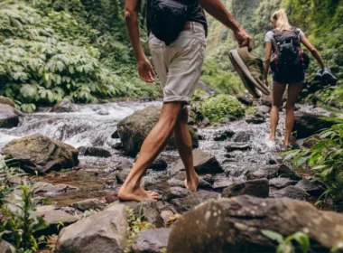 Two hikers take off their shoes to hike through a stream in search of a waterfall.