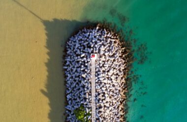 An aerial view of a pier jutting out to wear freshwater meets saltwater in the ocean, creating a visual boundary in the water of murky water and clear water.