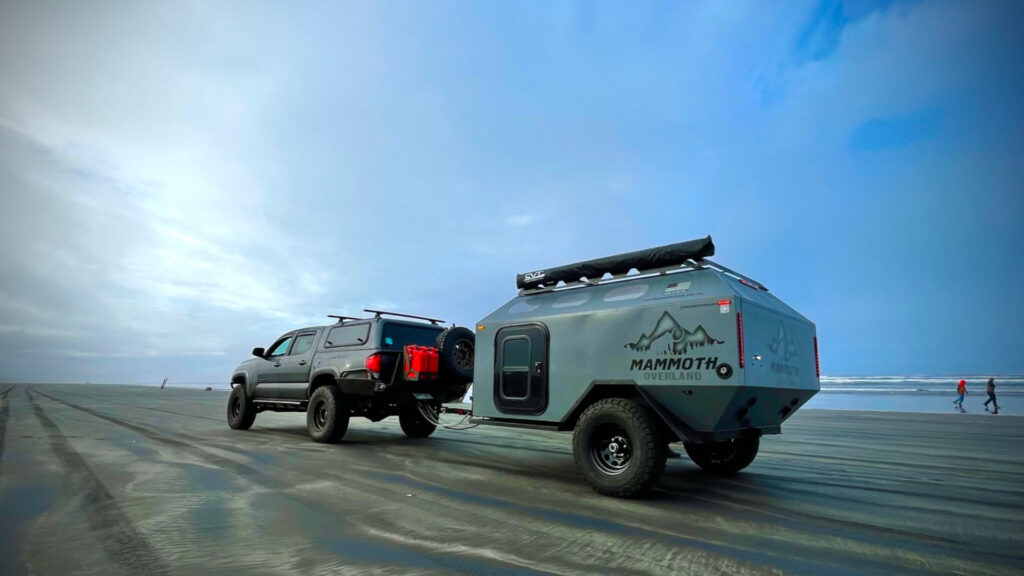 The back of a Mammoth Overland trailer attached to a truck driving on the beach