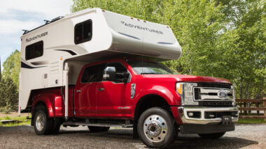An Adventure truck camper attached to a red pickup truck