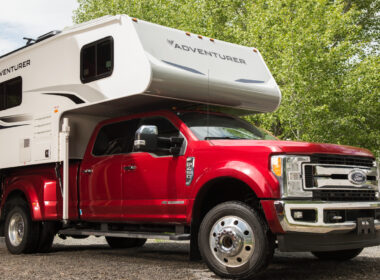 An Adventure truck camper attached to a red pickup truck