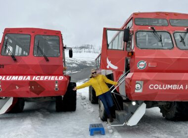 A couple smiling outside of guided tour buses at the Columbia Icefield Glacier Adventure