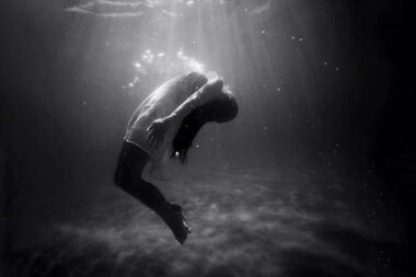 A woman underwater curving her back under the surface.