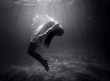 A woman underwater curving her back under the surface.