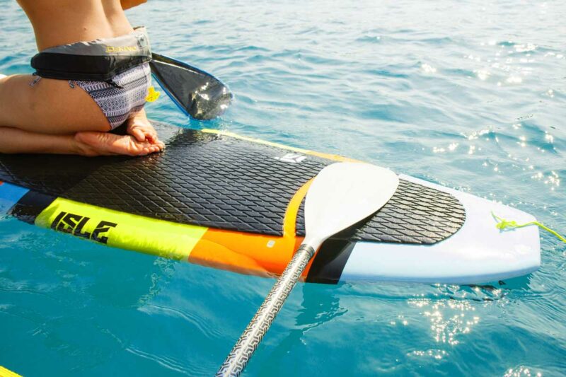 A paddle resting on a paddle board in aquamarine waters